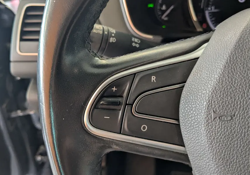 Gros plan sur les commandes au volant en cuir noir de la Renault Mégane IV 1.5 BlueDCI 115 EDC Intens, tableau de bord partiellement visible.