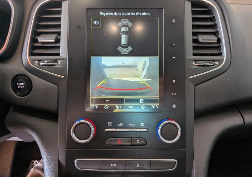 Vue rapprochée de la console centrale de la Renault Mégane IV gris, écran tactile affichant la caméra de recul et commandes climatisation.