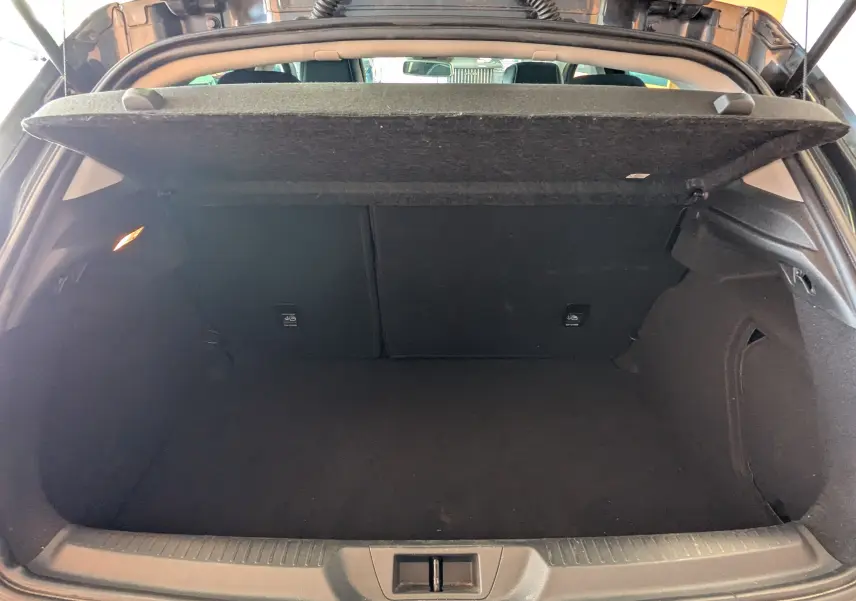 Coffre ouvert vu de l'arrière d'une Renault Mégane IV gris, montrant l'espace de chargement vide et la tablette cache-bagages relevée.