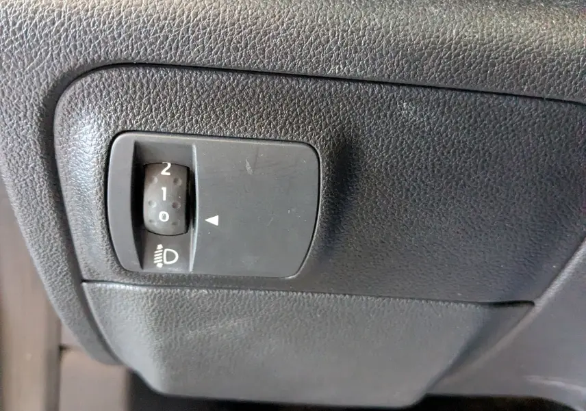 Gros plan sur le réglage d'inclinaison des phares dans l'habitacle noir de la Renault Mégane IV gris diesel.