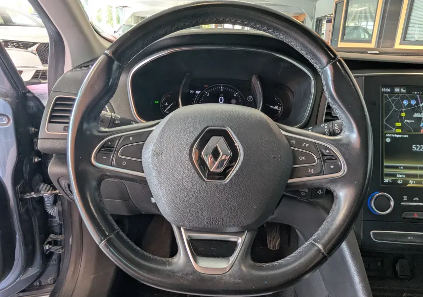 Vue centrée sur le volant en cuir noir de la Renault Mégane IV gris, avec tableau de bord et écran tactile visibles.
