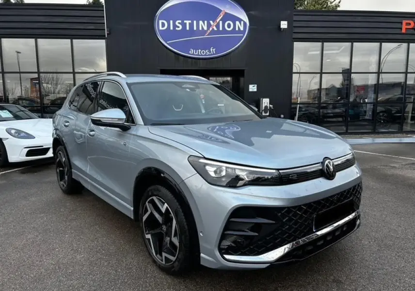 Volkswagen Tiguan III R-Line gris clair en 3/4 avant droit avec jantes alliage noires et calandre noire distinctive.