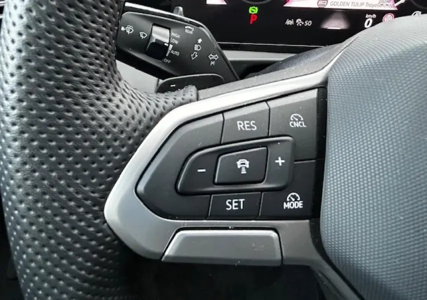 Gros plan sur les commandes de régulateur de vitesse au volant perforé du Volkswagen Tiguan gris clair 2024.