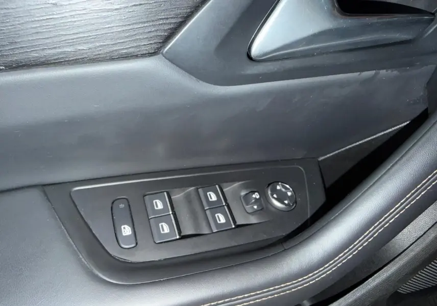 Gros plan sur les commandes de lève-vitres et rétroviseurs électriques sur la porte côté gauche en cuir noir.