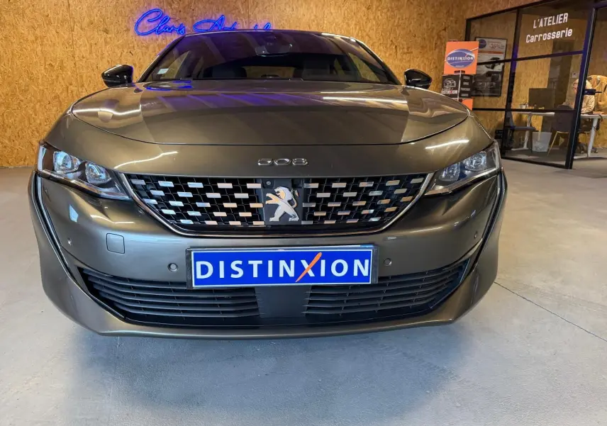 Vue frontale d'une Peugeot 508 gris métallisé avec calandre chromée et plaque Distinxion en intérieur d'atelier.