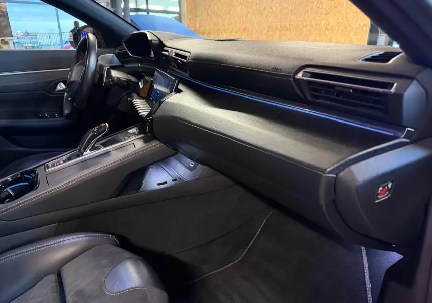 Intérieur avant droit de la Peugeot 508 gris, avec tableau de bord en bois, éclairage d'ambiance bleu et sellerie cuir noir.