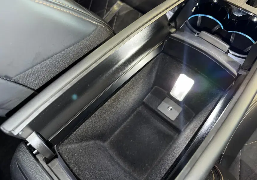 Vue rapprochée de l'accoudoir central ouvert en cuir noir de la Peugeot 508 II gris, avec compartiment de rangement éclairé.