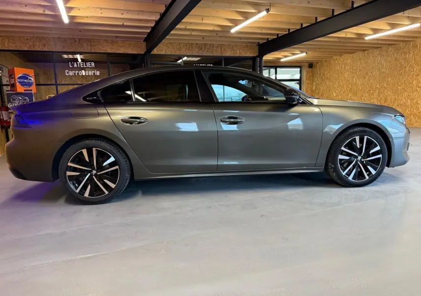 Profil droit d'une Peugeot 508 gris métallisé avec jantes alu noires et toit noir dans un garage.