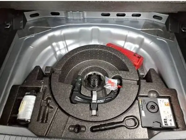 Vue plongeante sur le compartiment de rangement sous le coffre du Volkswagen T-Roc gris clair, montrant l’outillage et le kit de réparation.