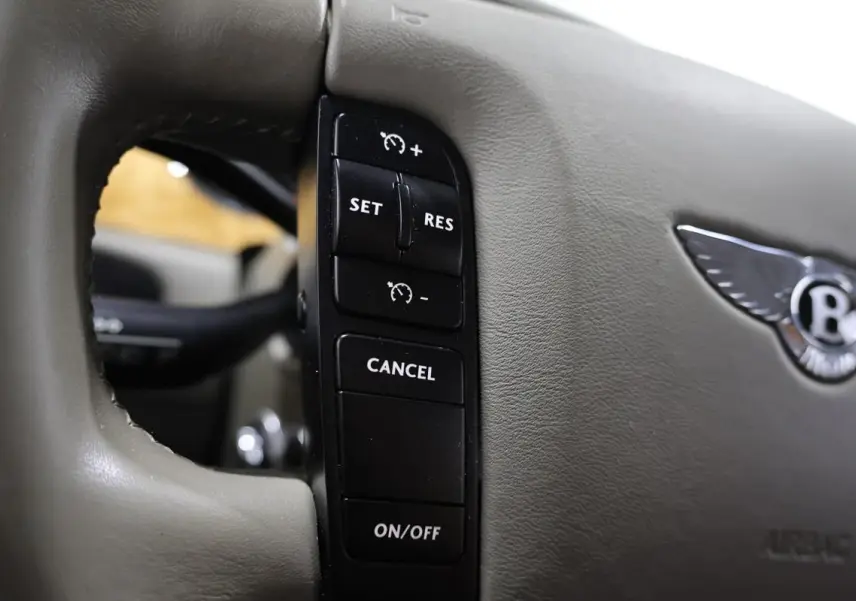 Gros plan sur les commandes de régulateur de vitesse sur le volant beige clair d'une Bentley Continental Flying Spur.
