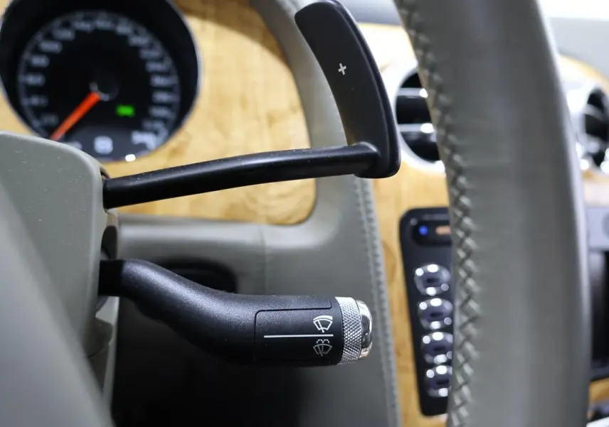Gros plan sur la commande d’essuie-glace noire et volant cuir gris dans l’habitacle bois clair d’une Bentley Continental Flying Spur.