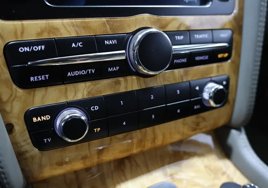 Gros plan sur la console centrale en bois clair avec commandes audio et navigation de la Bentley Continental Flying Spur.