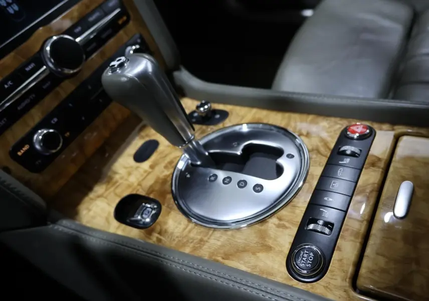 Gros plan sur la console centrale en bois clair de la Bentley Continental Flying Spur, avec levier de vitesse automatique et boutons de commande.