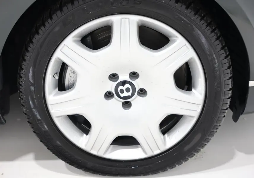 Gros plan sur la jante blanche avec logo Bentley noir, montée sur un pneu noir, partie avant droite du Bentley Continental Flying Spur vert foncé.