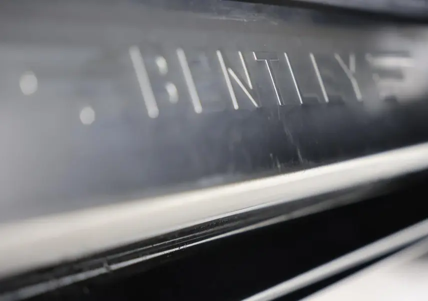 Gros plan sur la plaque de seuil de porte en métal gravé "BENTLEY" sur une Bentley Continental Flying Spur vert foncé.
