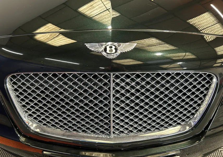 Gros plan sur la calandre chromée et l'emblème Bentley d'une Continental Flying Spur vert foncé, vue de face.