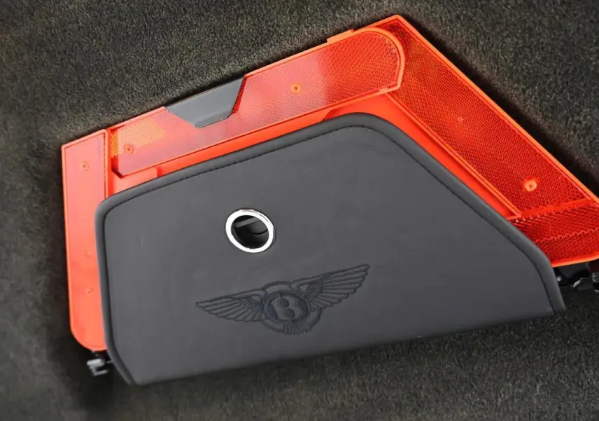 Détail du coffre avec triangle de sécurité rouge et housse noire siglée Bentley sur un Continental Flying Spur vert foncé.