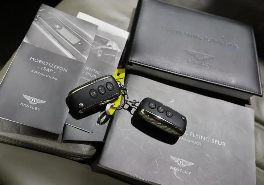 Vue rapprochée sur les clés et les manuels noirs du Bentley Continental Flying Spur posés sur un siège en cuir gris.
