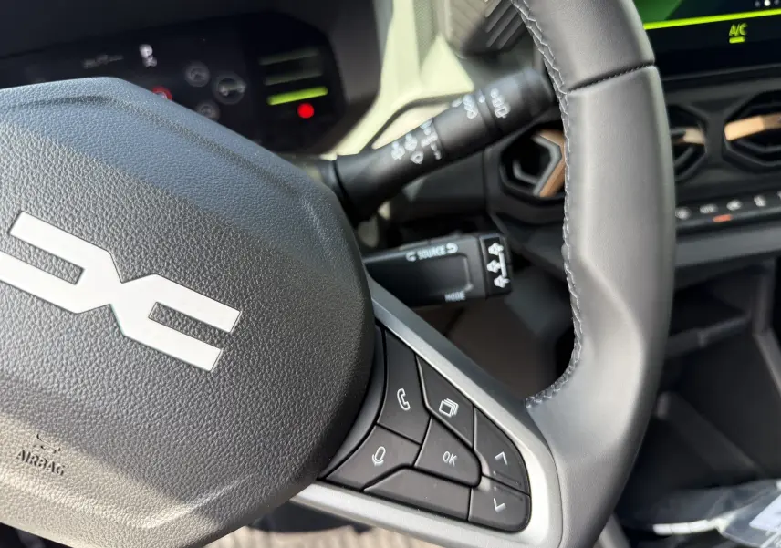 Gros plan sur le volant gris du Dacia Duster Hybrid 155 Extreme 2026, avec commandes intégrées et tableau de bord partiellement visible.