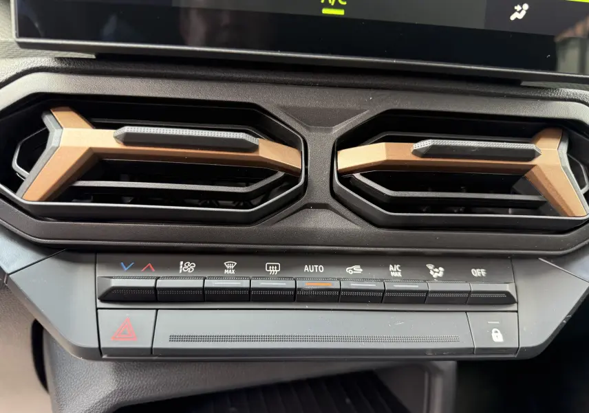 Gros plan sur les aérateurs et commandes de climatisation du tableau de bord du Dacia Duster Hybrid 155 Extreme blanc glacier 2026.