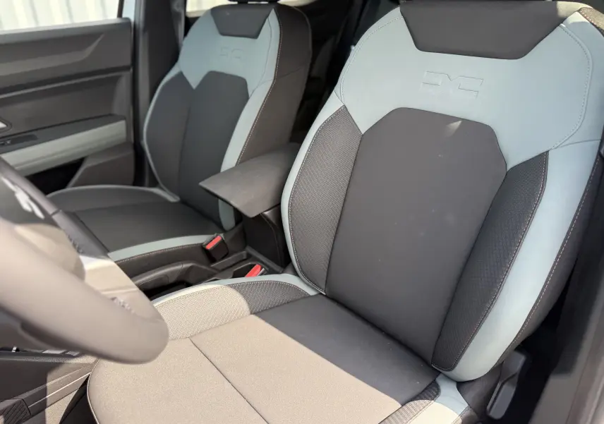 Vue rapprochée des sièges avant tissu noir et gris clair du Dacia Duster Hybrid 155 Extreme 2026, avec accoudoir central.