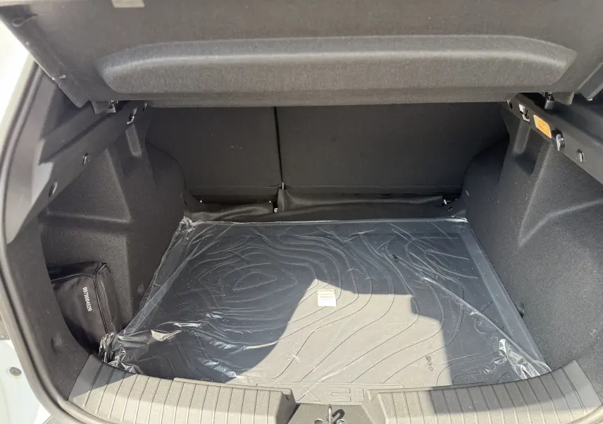 Coffre ouvert du Dacia Duster Hybrid 155 Extreme blanc glacier, montrant un tapis de protection noir et un rangement latéral.