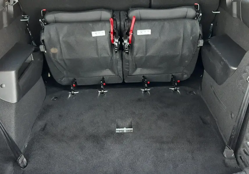 Vue arrière du coffre du Dacia Jogger 2025, sièges rabattus en tissu noir avec sangles rouges visibles.