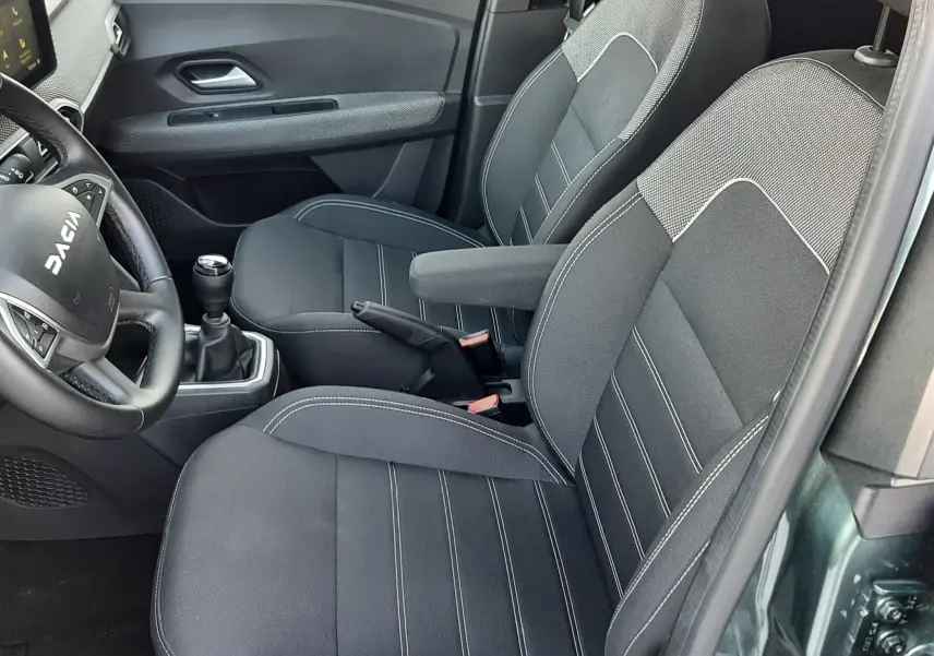 Vue intérieure côté conducteur du Dacia Jogger 2025 vert cèdre, sièges tissu noir avec coutures blanches et volant multifonction.