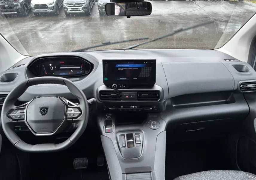 Vue intérieure avant du Peugeot Rifter gris Artense 2026, tableau de bord moderne avec écran tactile central et volant multifonctions cuir.