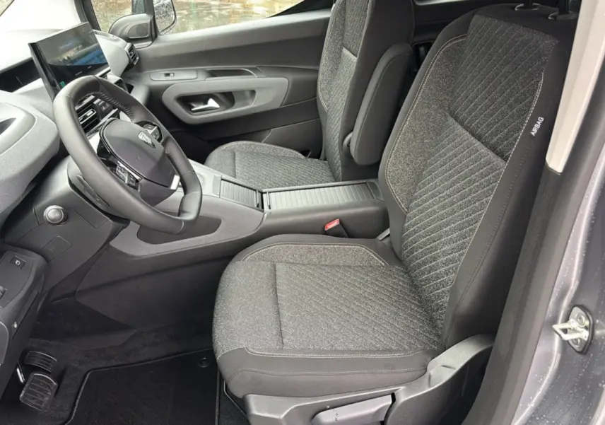 Vue intérieure côté conducteur du Peugeot Rifter 2026, sièges tissu gris et volant cuir multifonctions.