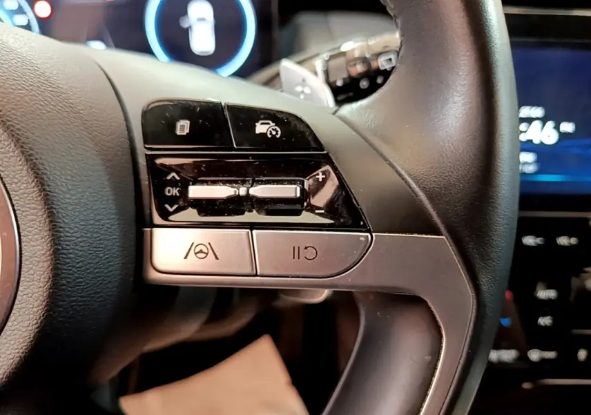 Gros plan sur le volant cuir noir du Hyundai Tucson 1.6 Hybrid 2022, avec commandes multifonctions et affichage digital en arrière-plan.