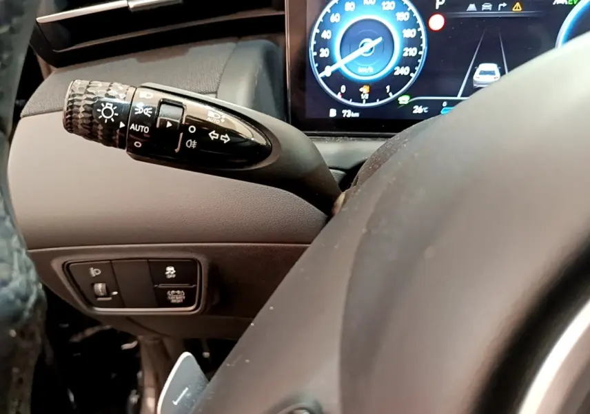 Gros plan sur la manette de clignotants et le tableau de bord numérique bleu du Hyundai Tucson 1.6 Hybrid 230 Creative.