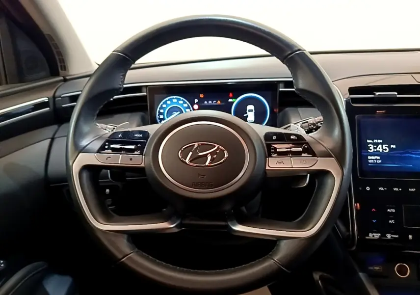 Vue frontale du volant en cuir noir du Hyundai Tucson 1.6 Hybrid 230 avec tableau de bord numérique et écran tactile central.