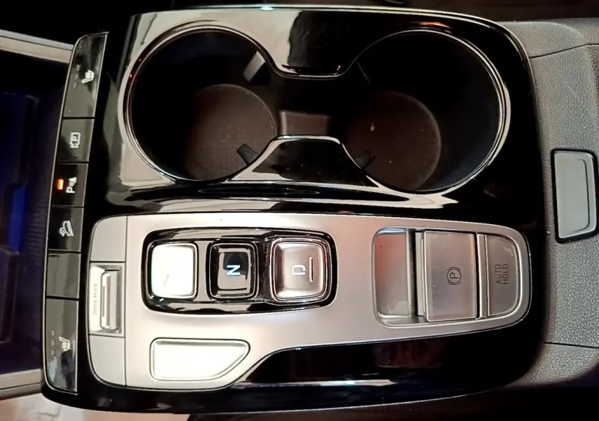 Gros plan sur la console centrale noire et argentée du Hyundai Tucson 1.6 Hybrid 230, avec commandes de boîte auto et porte-gobelets.