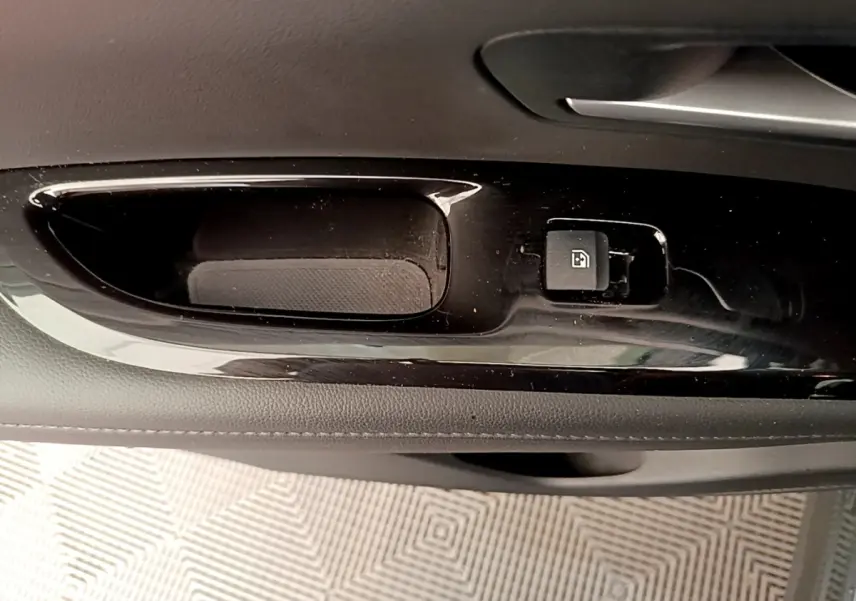 Gros plan sur la poignée intérieure noire de la porte avant droite du Hyundai Tucson gris foncé, bouton de verrouillage visible.