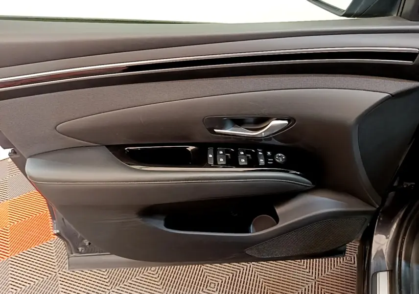 Vue intérieure côté gauche de la porte avant d’un Hyundai Tucson gris foncé, avec commandes de vitres et poignée argentée.