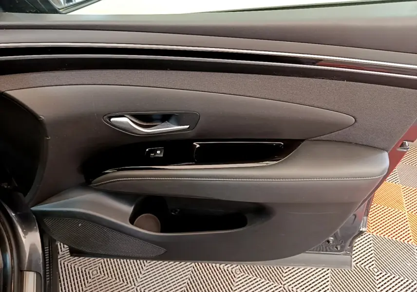 Vue intérieure sur la porte avant gauche d’un Hyundai Tucson gris foncé, avec poignée argentée et accoudoir noir.