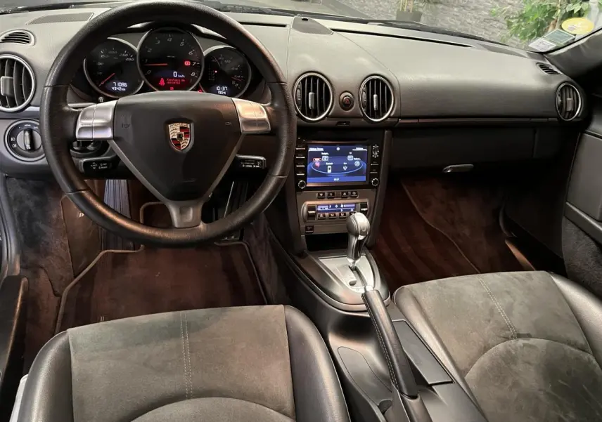 Intérieur noir de Porsche Cayman 987 2008, vue frontale sur volant, tableau de bord et console centrale avec levier automatique.