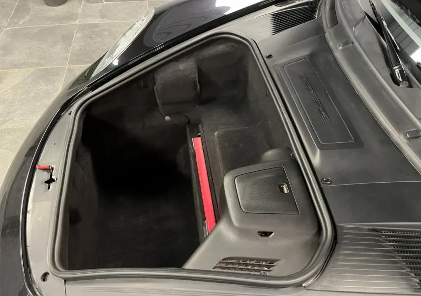 Vue plongeante sur le coffre avant noir ouvert d'une Porsche Cayman 987 2.7i avec intérieur propre et compartiments visibles.