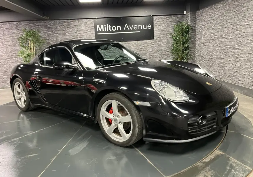 Porsche Cayman noir vue 3/4 avant droit avec jantes 18 pouces et étriers de frein rouges dans un showroom.
