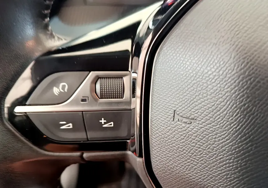 Gros plan sur les commandes gauche du volant cuir noir de la Peugeot 208 PureTech blanche, version 2020.