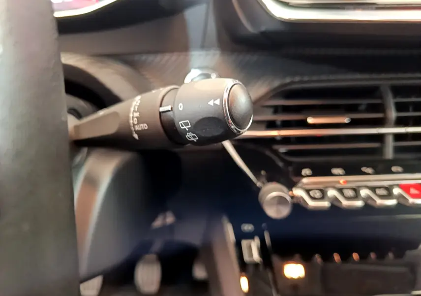 Gros plan sur la commande d’essuie-glace à gauche du volant dans l’habitacle sombre d’une Peugeot 208 blanche 2020.
