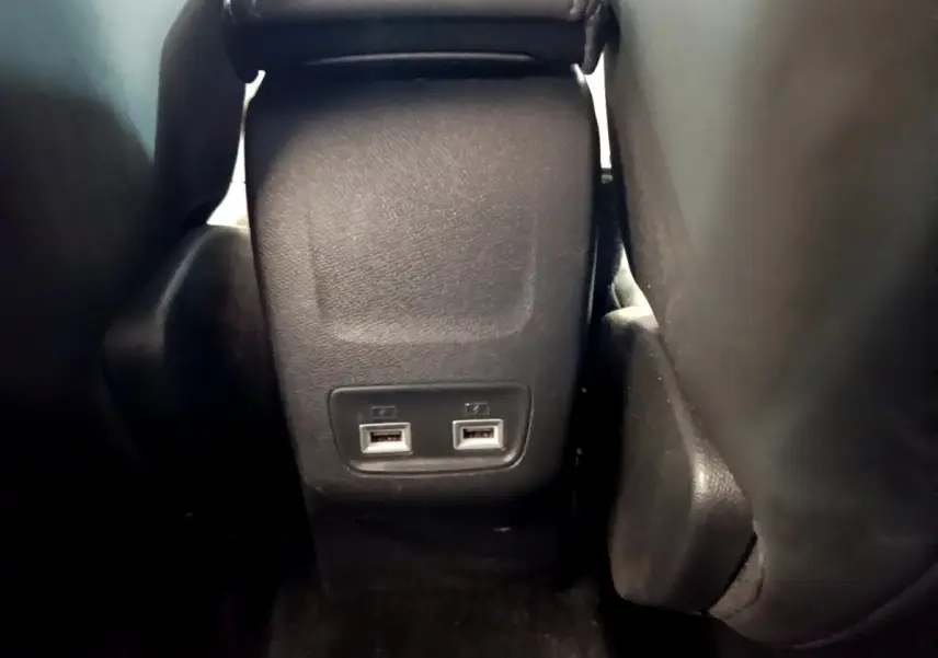 Vue rapprochée des ports USB arrière entre les sièges noirs de la Peugeot 208 PureTech 100 S&S Allure Business blanche.