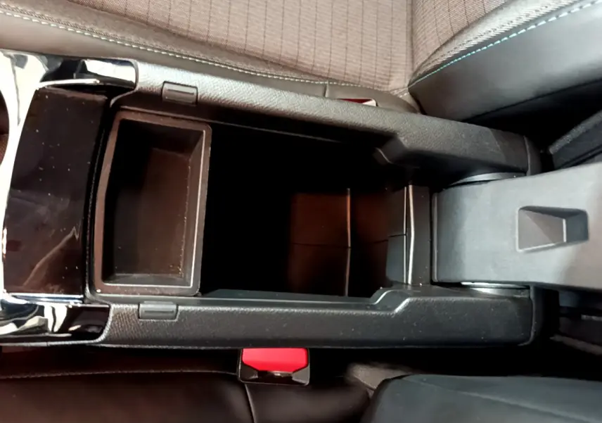 Vue plongeante sur la console centrale noire ouverte du Peugeot 208 blanc, montrant le rangement intérieur et le frein à main électrique.