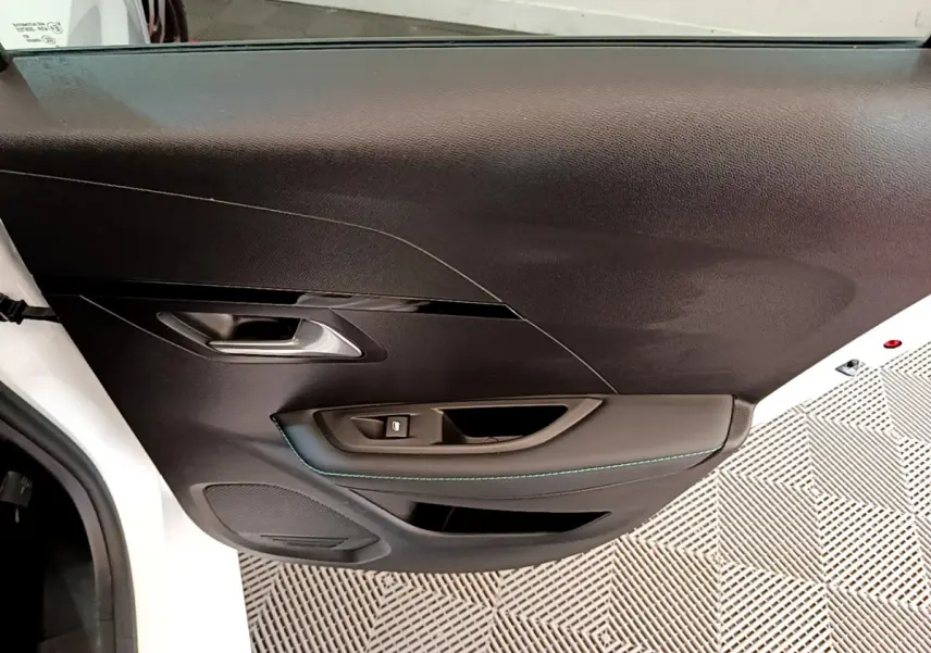 Vue rapprochée de la porte avant gauche noire de la Peugeot 208 blanche, avec poignée et commande de vitre intégrées.