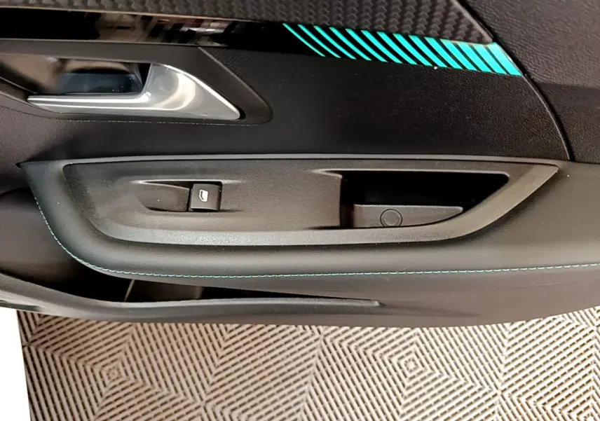 Détail de la porte intérieure côté conducteur de la Peugeot 208 blanche avec surpiqûres bleues et poignée argentée.