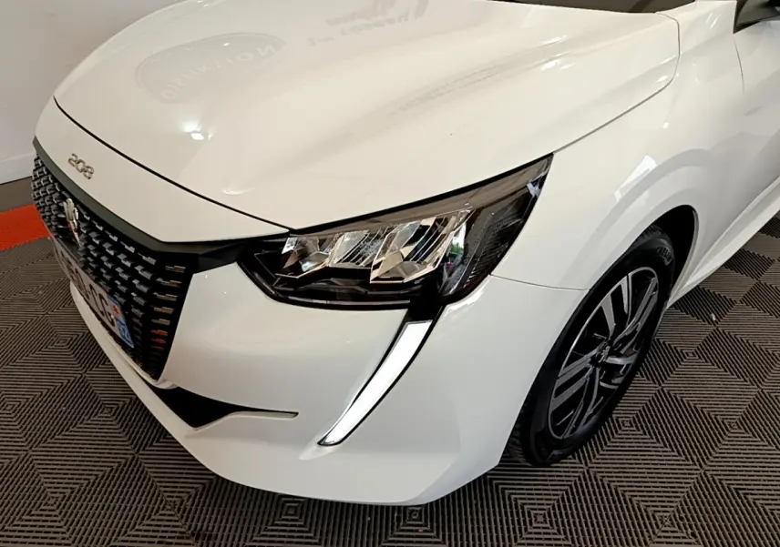 Vue 3/4 avant droit d'une Peugeot 208 blanche avec phares LED et calandre noire distinctive.