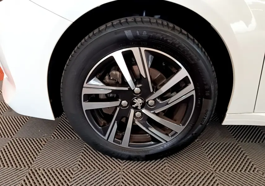 Gros plan sur la roue avant gauche blanche d'une Peugeot 208 PureTech 100 S&S Allure Business avec jante alliage noire et argent.