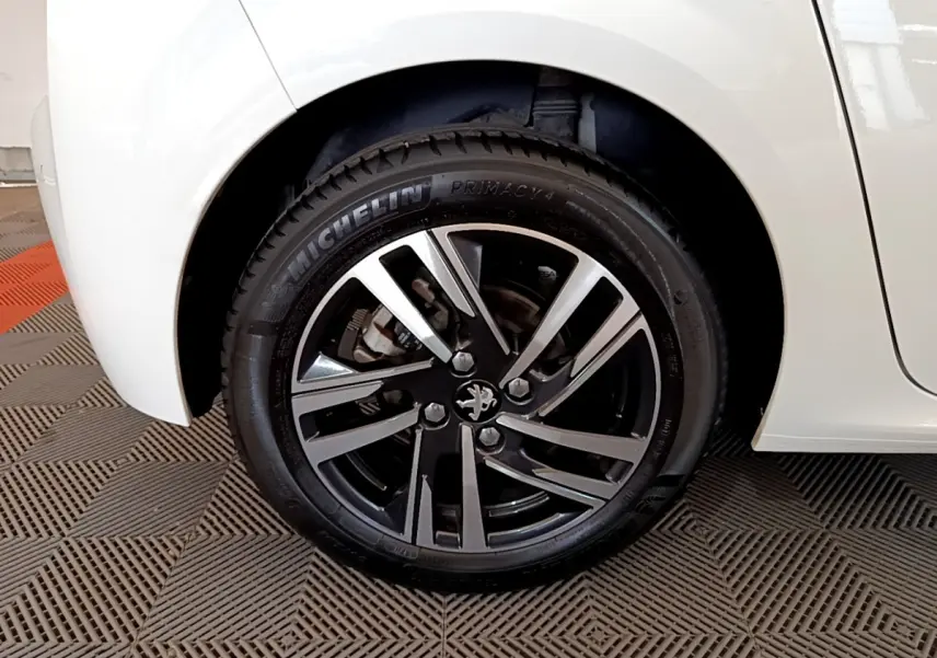 Gros plan sur la roue arrière droite blanche d'une Peugeot 208 PureTech 100 S&S Allure Business avec jante alliage noire et argent.