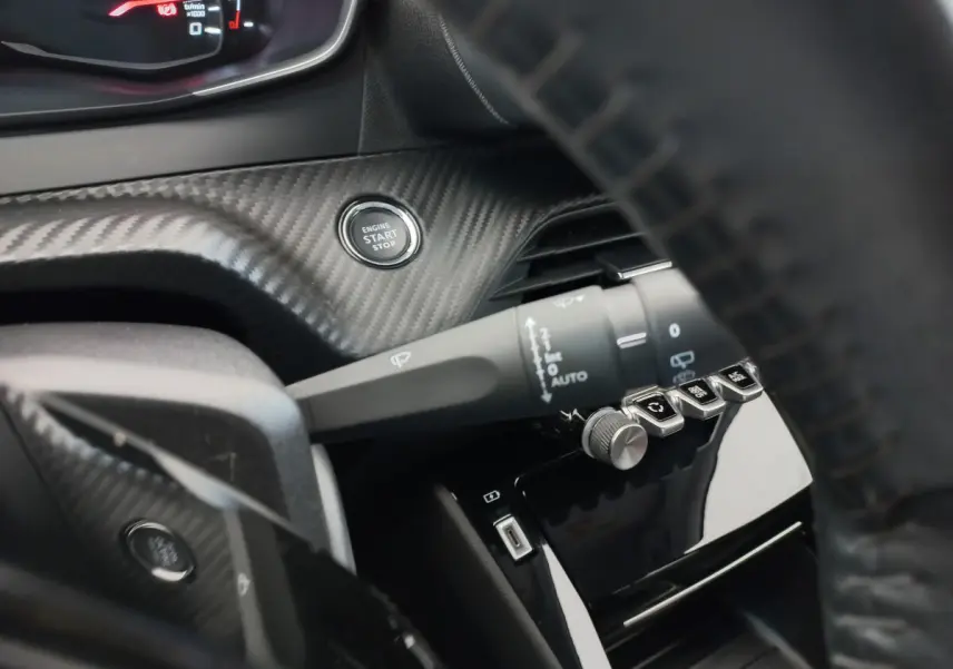 Gros plan sur le bouton start/stop et la commande d'essuie-glace dans l'habitacle noir du Peugeot 208 PureTech 100 S&S Allure 2021.